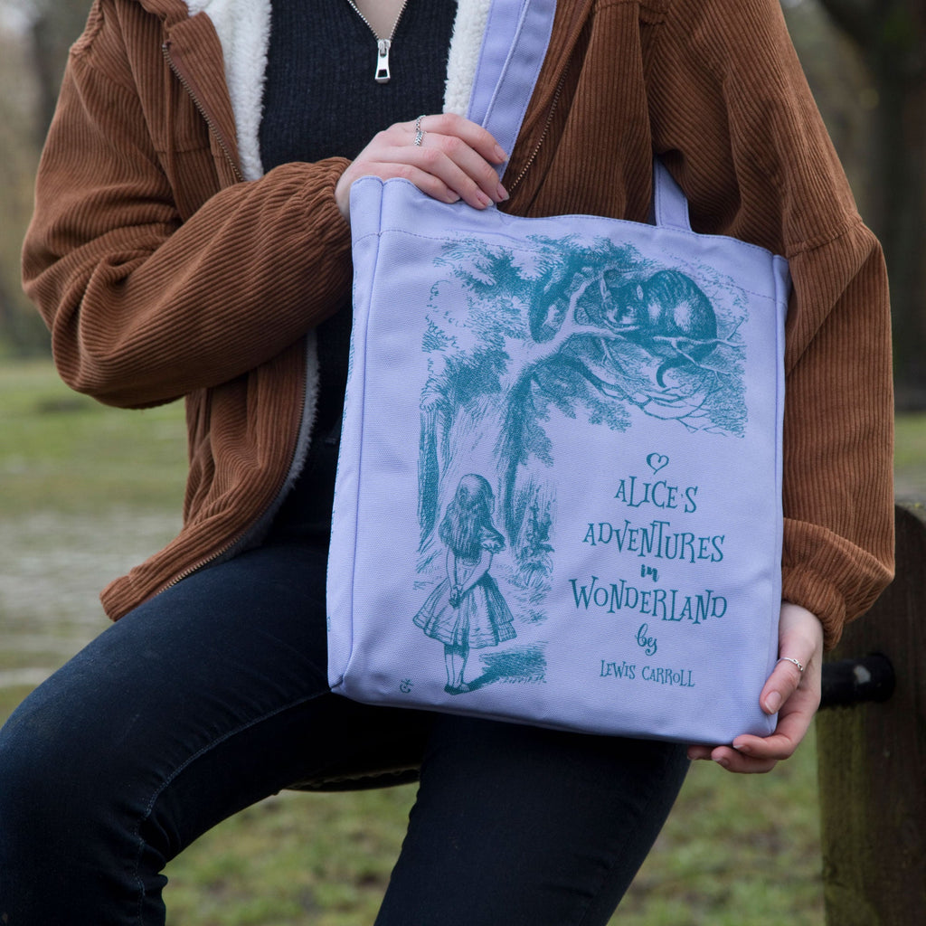 Alice's Adventures in Wonderland Purple Tote Bag by Lewis Carroll featuring Alice and Cheshire Cat design, by Well Read Co. - Model Sitting with Bag
